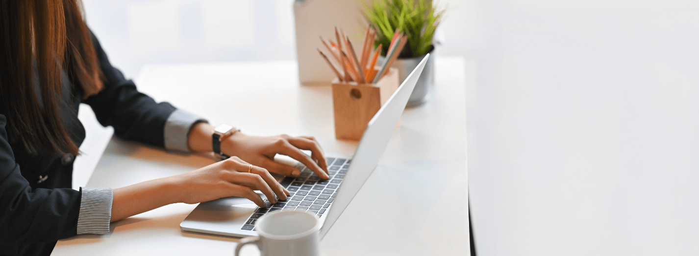 woman creating content, typing on a laptop, with a coffee mug on her desk.