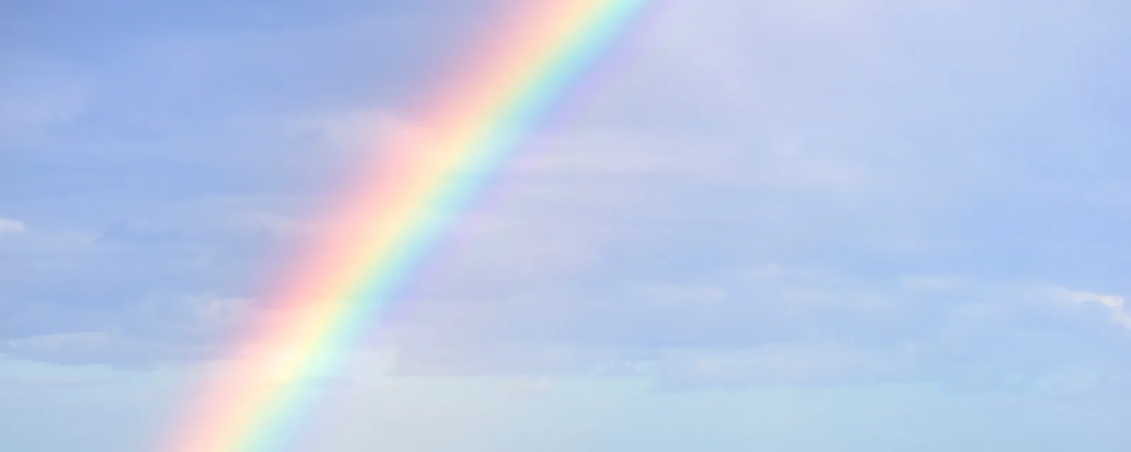 A rainbow arcing across a pale blue sky scattered with soft cloud.