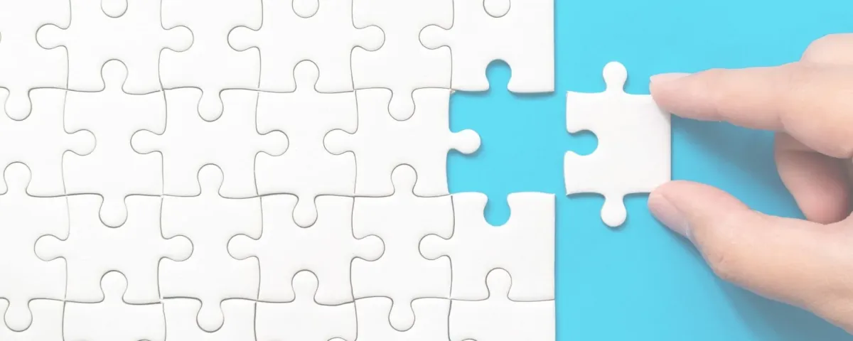 A hand placing the final white jigsaw piece into a completed puzzle on a blue background.