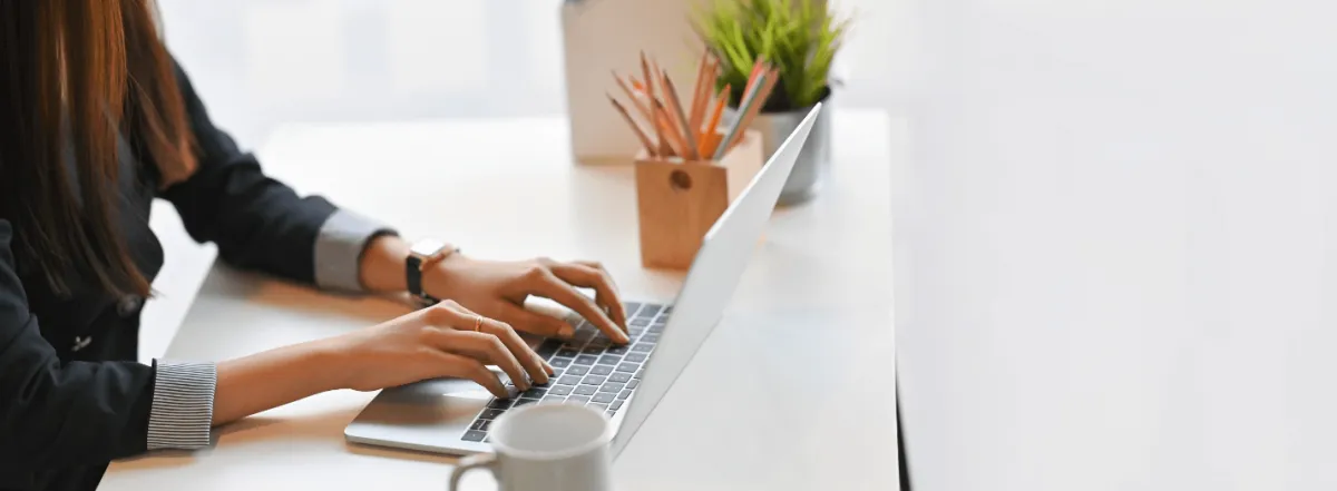 woman creating content, typing on a laptop, with a coffee mug on her desk.