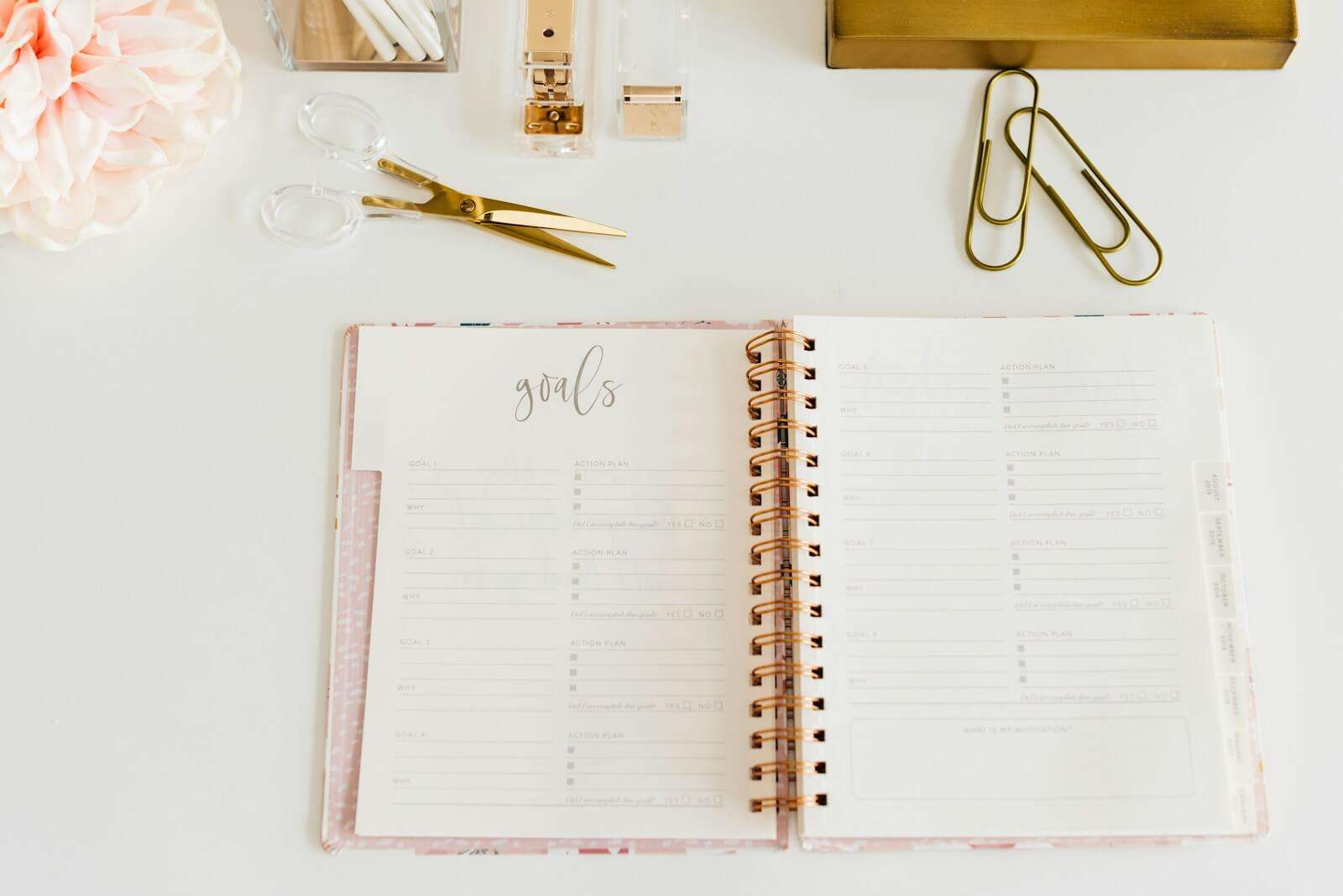 scissors and two paper clips beside opened spiral notebook with the word GOALS at the top