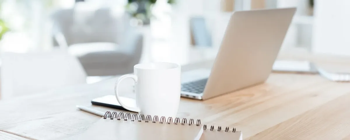 still life photo of a laptop, mug, and notebook