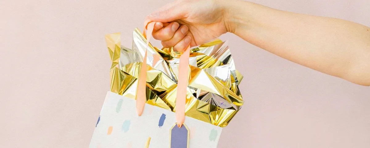 person holding a gift bag with gold tissue for blog post "9 No-Cost and Low-Cost Ways to Show Your Clients Love & Appreciation"
