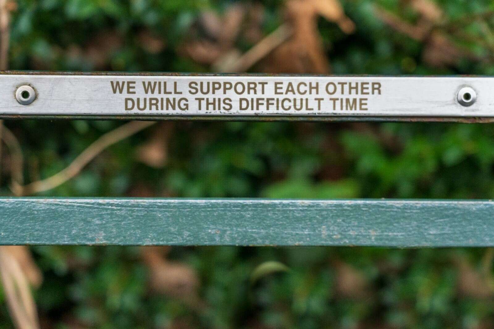 brown wooden bench with quote "we will support each other during this difficult time."
