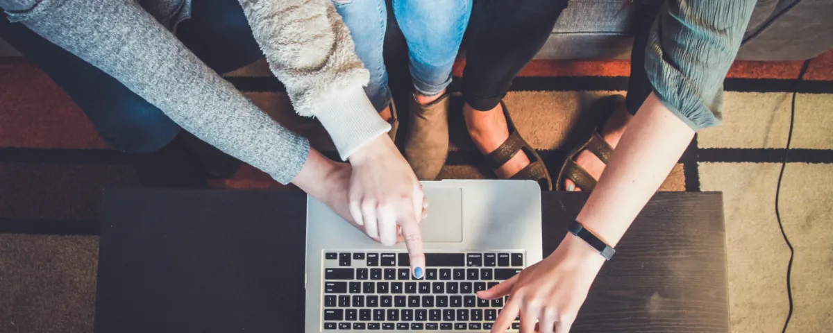 The hands of three people pointing at a laptop