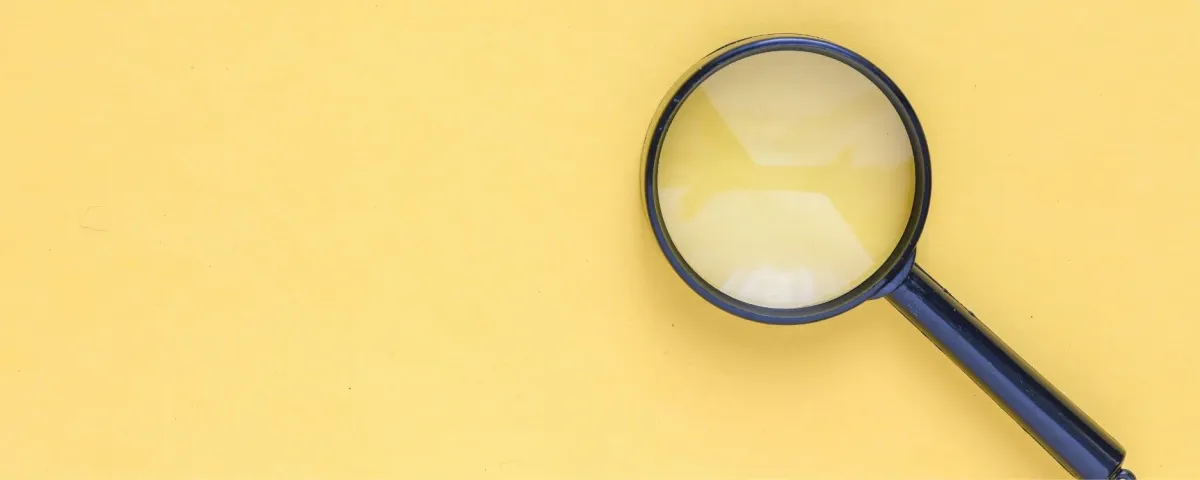 A single magnifying glass lying on a plain yellow background.