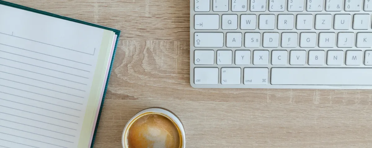 A notepad, keyboard, and coffee cup ready to write a blog post