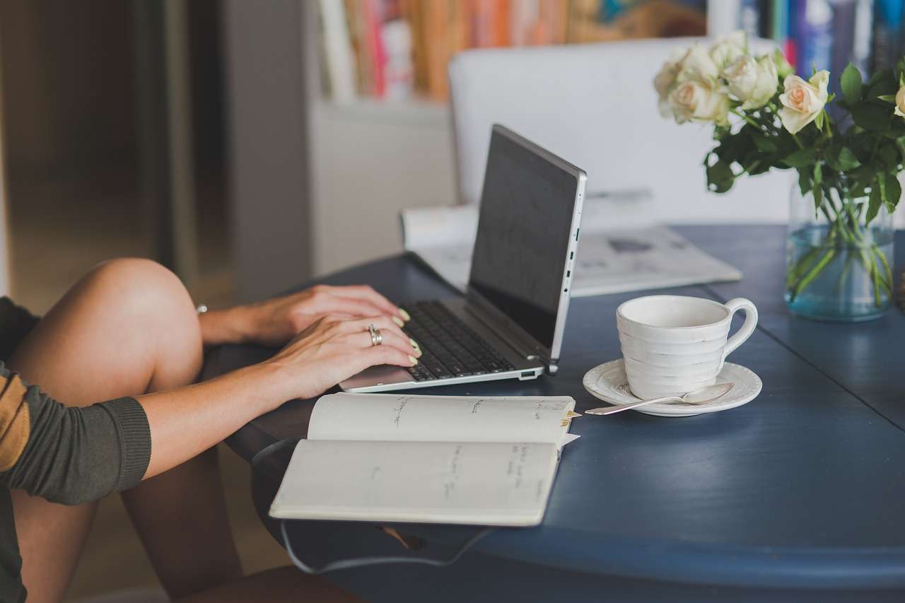 Woman typing on computer with journal and a cup of tea: 9 steps to create long-form content that converts for coaches