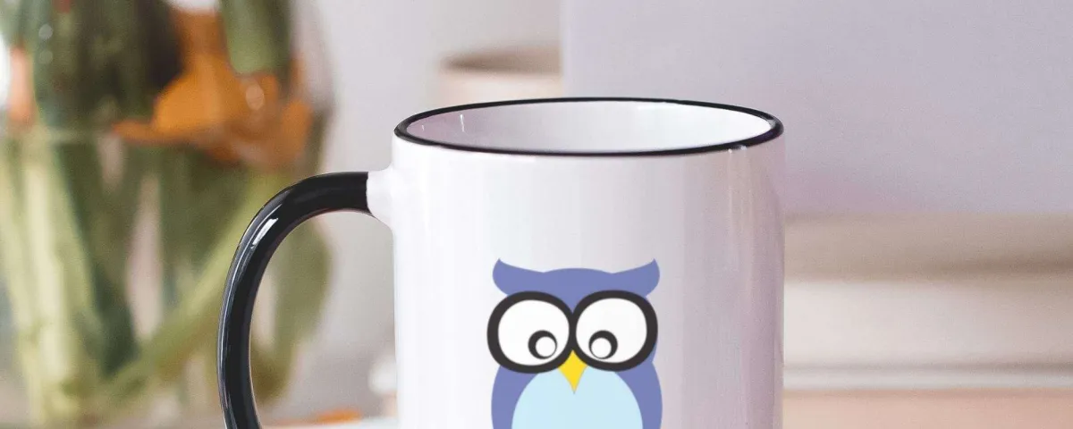 A white mug printed with the Wise Owl Marketing owl, on a desk beside a plant.
