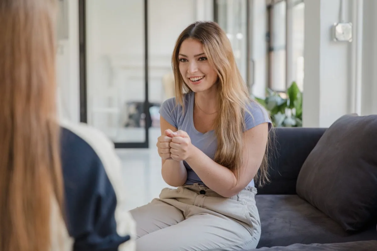 A coach and client in conversation on a sofa, one listening while the other talks with her hands.