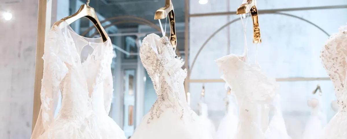 A row of white wedding dresses hanging on gold hangers in a bridal boutique.