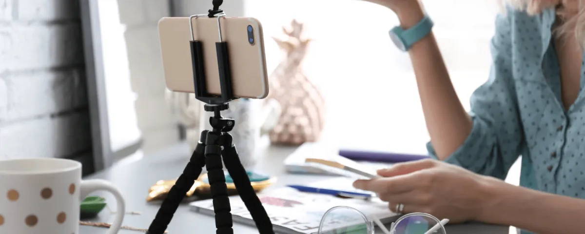 image of a phone in a tripod on a desk with a woman in the background recording a video