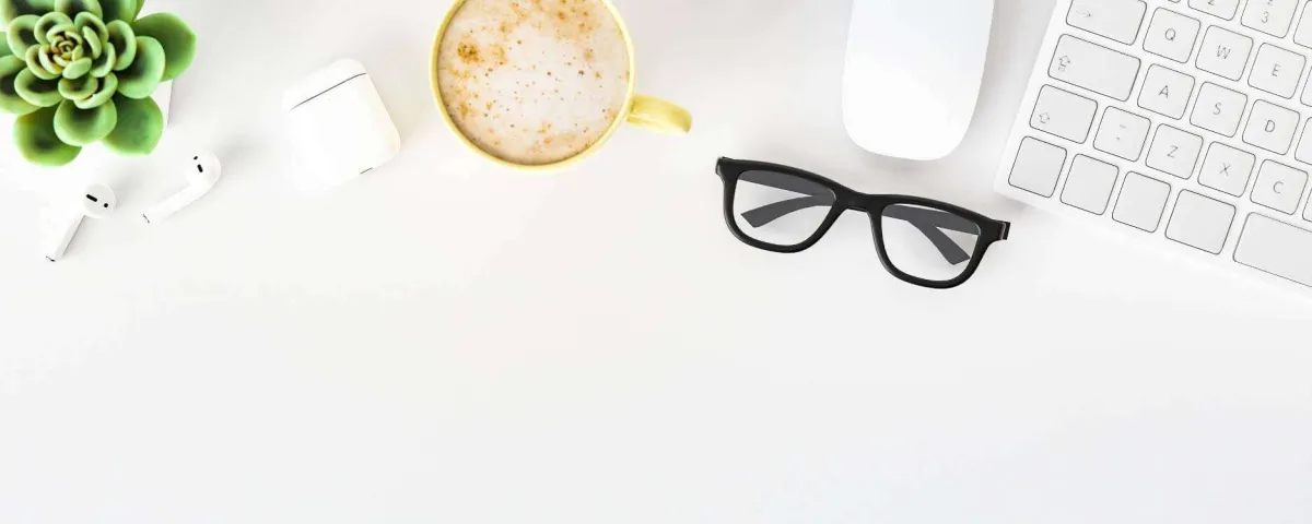 high-key flat lay of a desk with a keyboard, mouse, cappuccino, plant, and eyeglasses