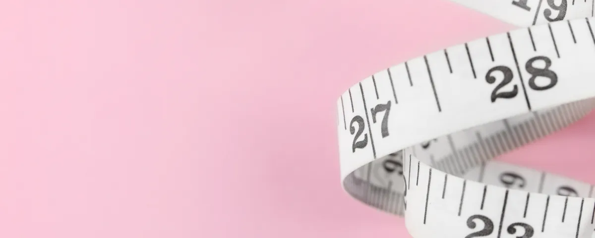A white flexible tape measure on a pink background representing measuring your marketing metrics.