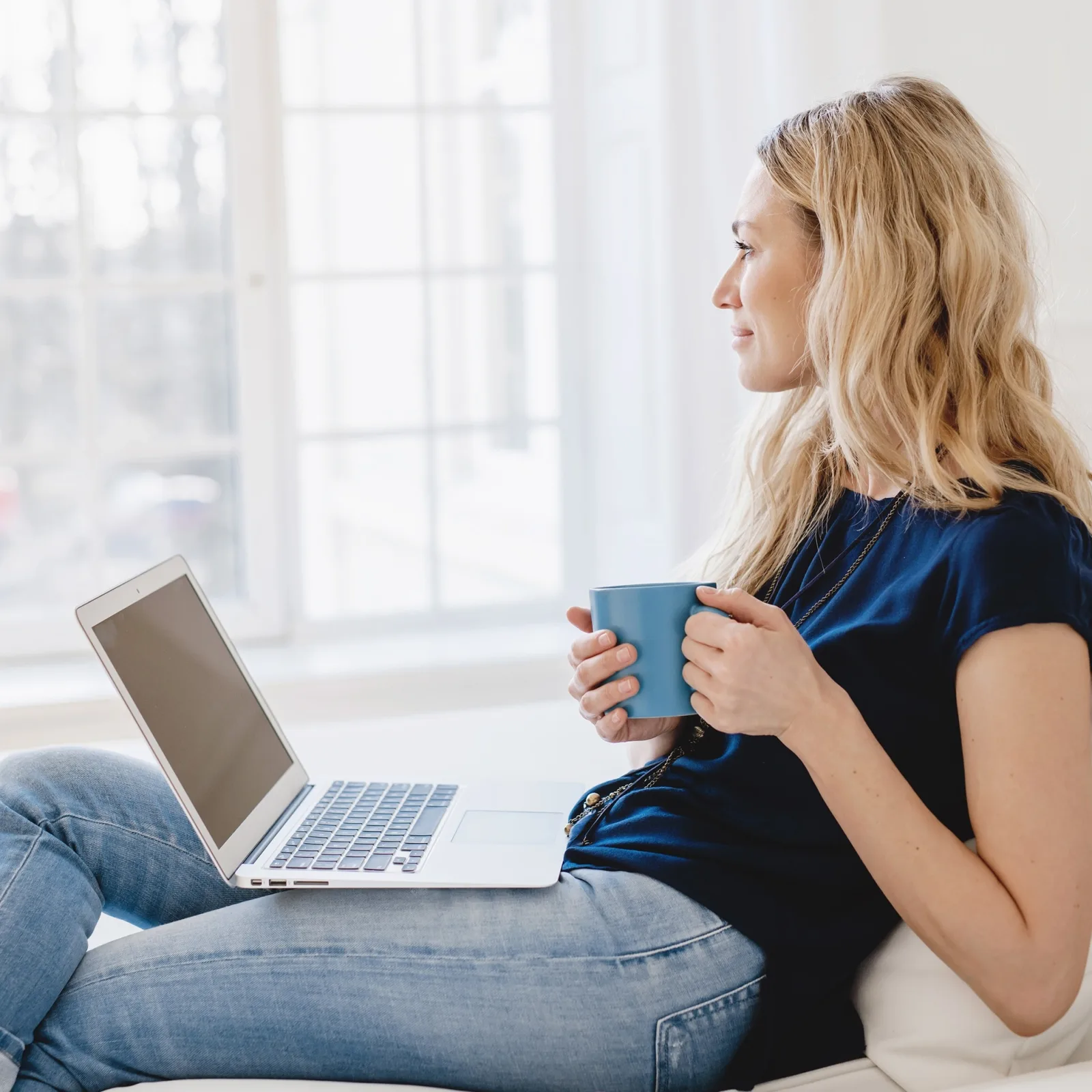 Woman with coffee and laptop gazing out the window day dreaming.