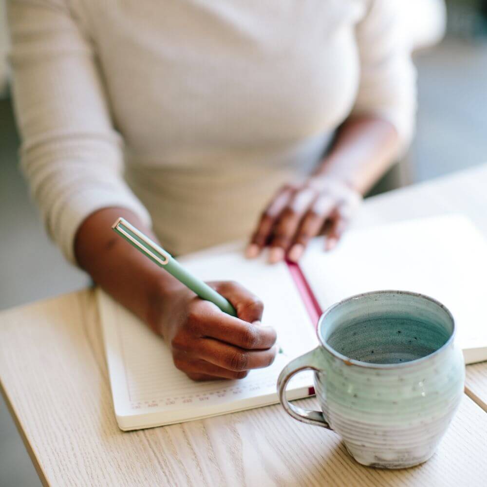 woman journaling with a aqua colored mug on the table