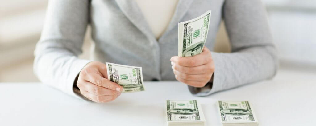 woman wearing a gray sweater counting money into piles on a desk