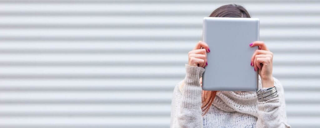 woman holding a laptop or an ipad against her face, hiding behind it.