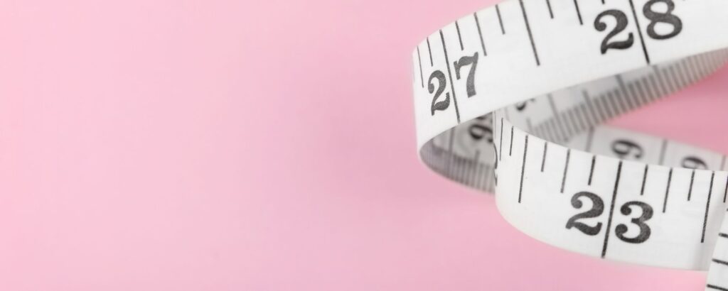 flexible tape measure curled in a ribbon spiral on a pink background