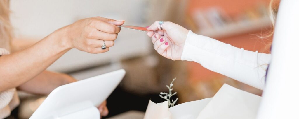 one woman handing a credit card to another woman at a checkout counter