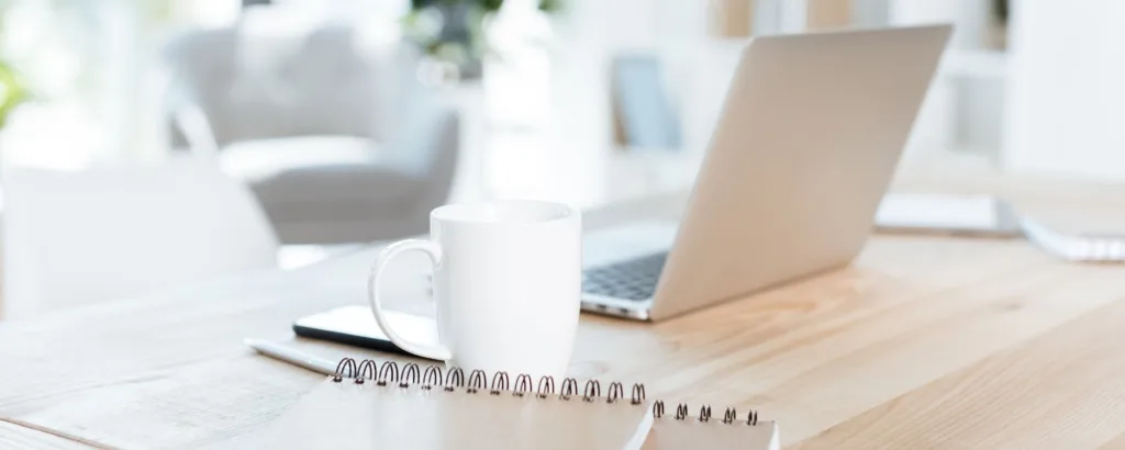 still life photo of a laptop, mug, and notebook