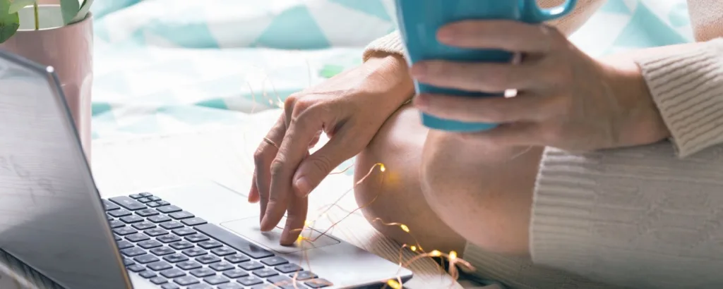 woman sitting on the floor typing on a laptop with one hand and holding a turquoise coffee mug with the other hand