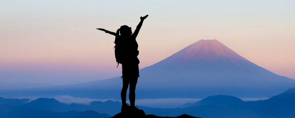 Woman wearing a backpack looking out at purple mountains with her arms up showing success