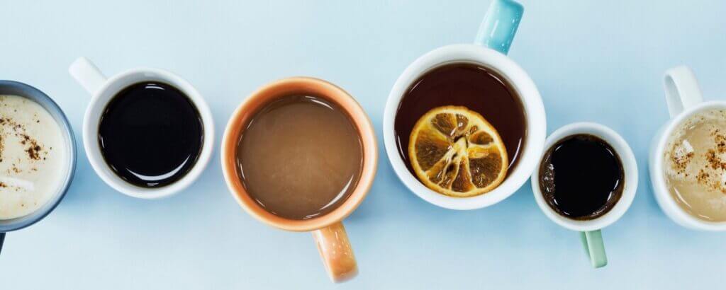 a row of 6 mugs on a blue table photographed from above with different types of drinks inside each mug