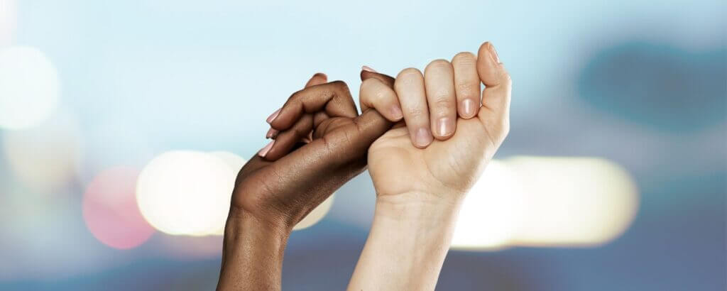 image of two women doing a pinky promise against a blurry blue background