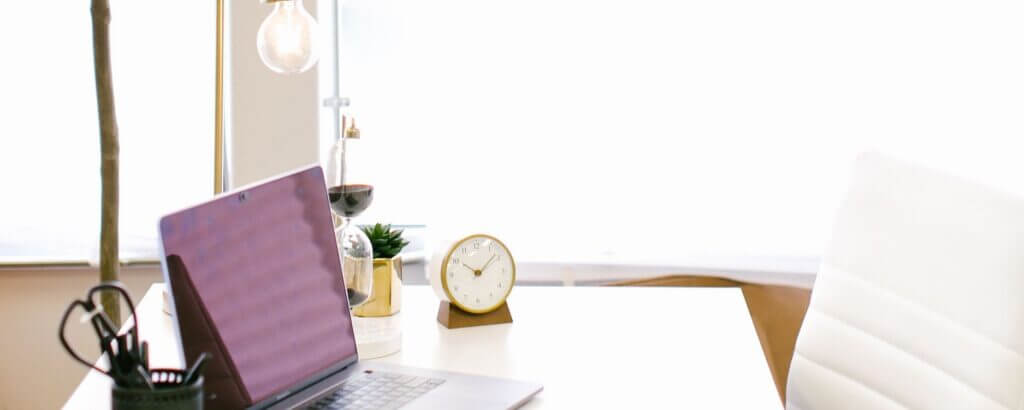 pretty desk in front of a window with a laptop, clock, white desk chair, etc.