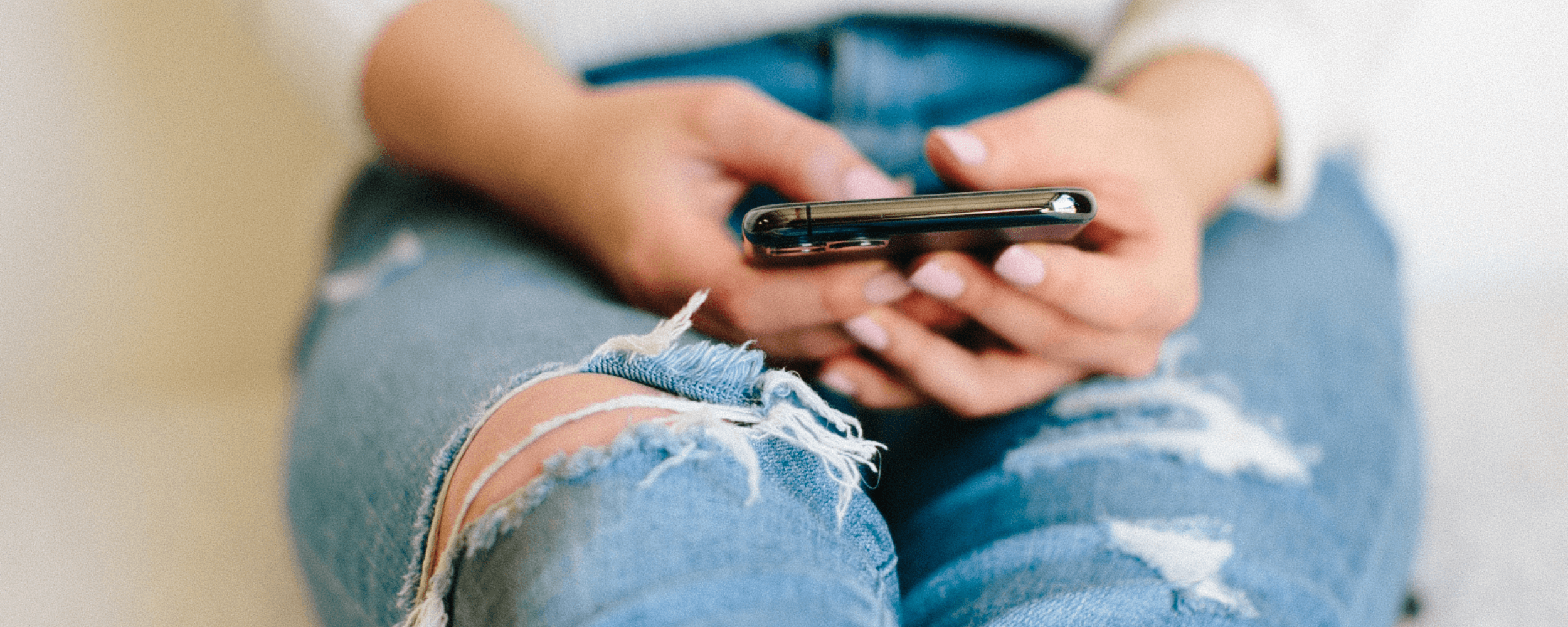 woman sitting on the floor in bluejeans holding her cell phone checking her email
