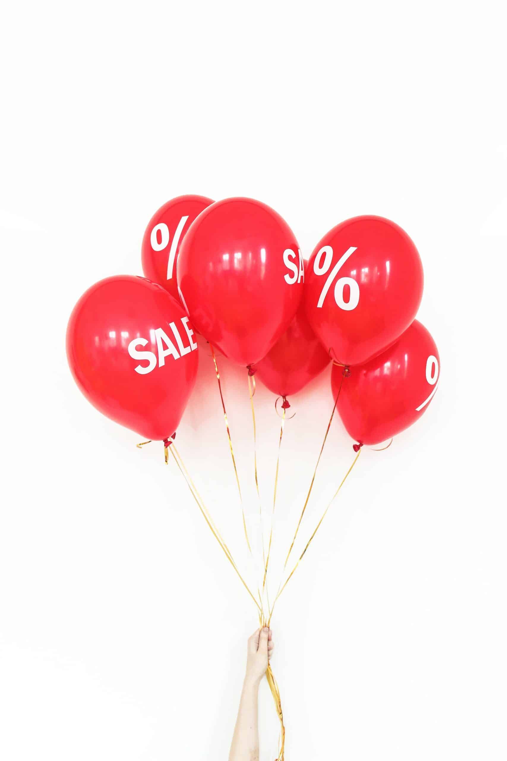 Woman holding a bunch of red balloons with the word Sale on them.