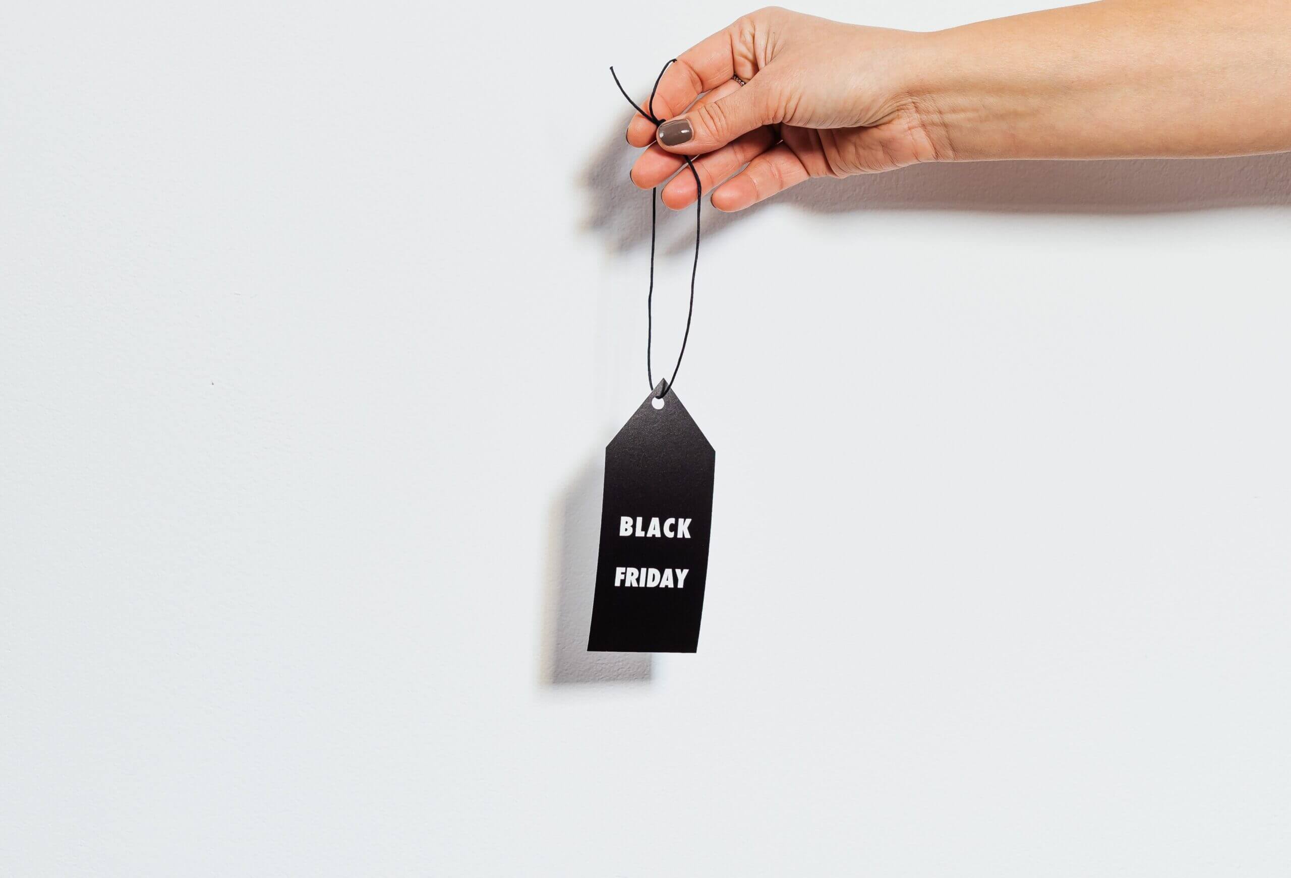 hand of a caucasian woman holding a black sales tag that says black Friday in white lettering.