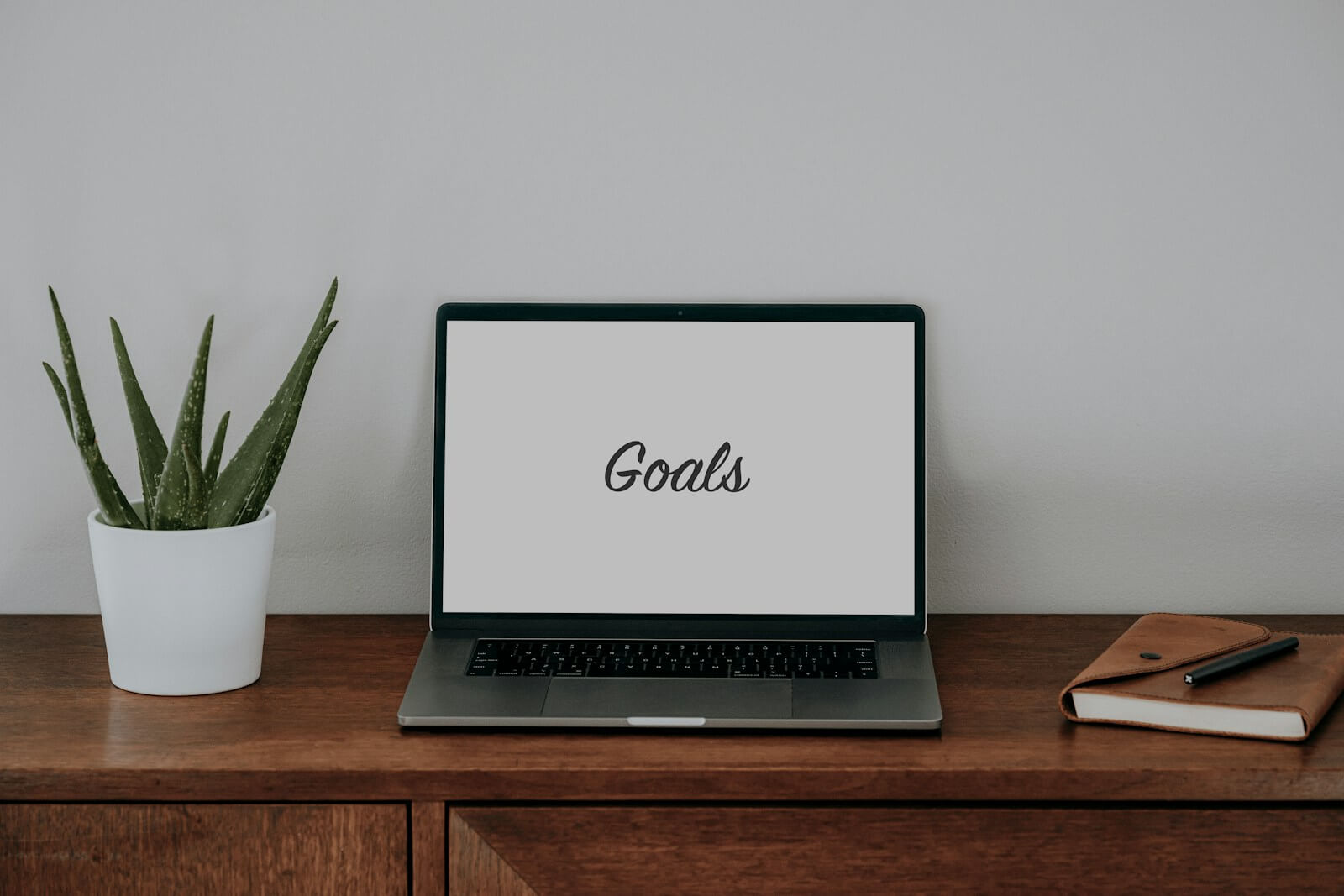 a laptop computer sitting on top of a wooden desk with the word Goals on the screen