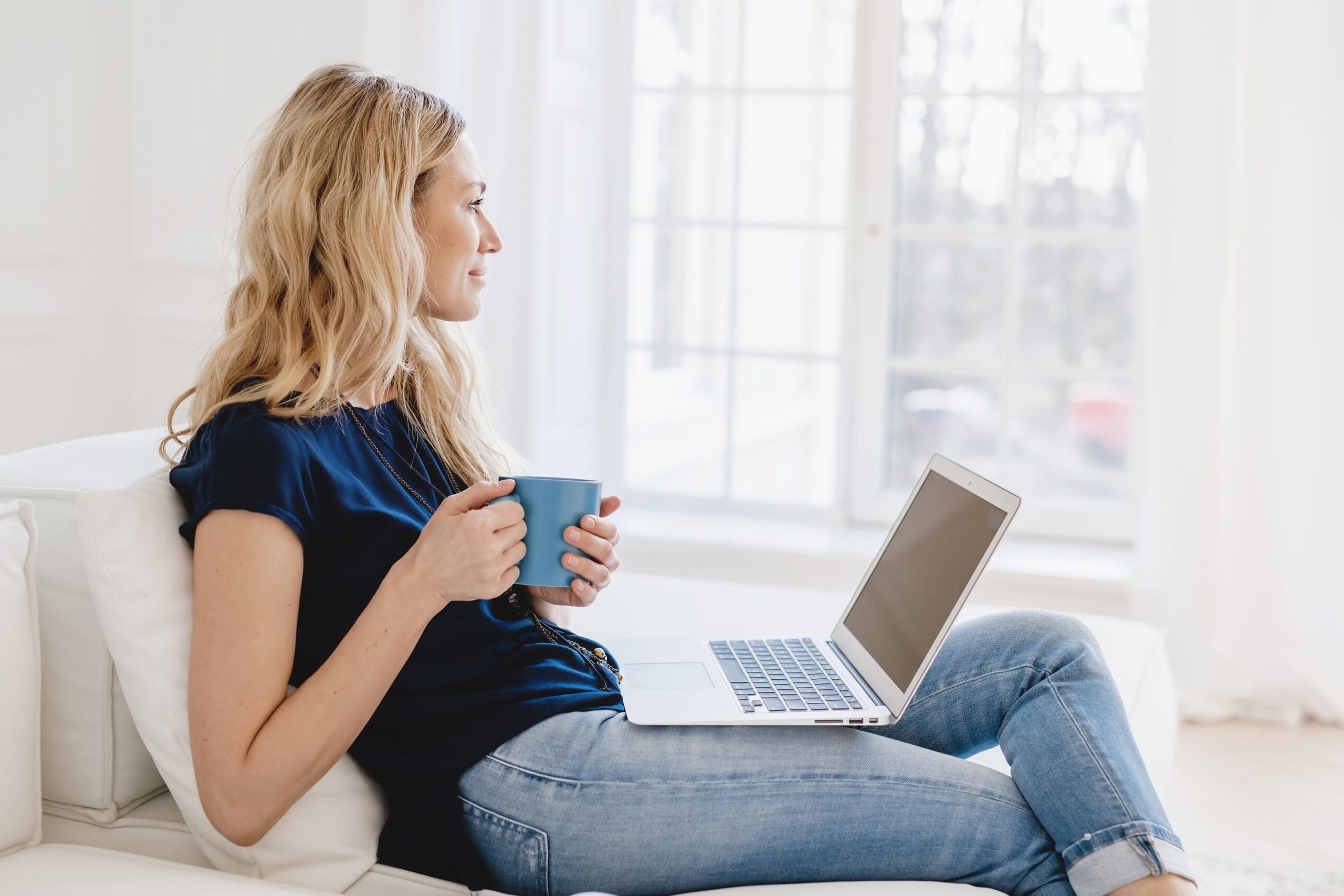 Woman sitting peacefully with her open holding coffee gazing out the window.