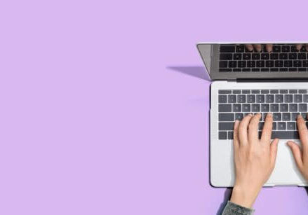 purple desk with a laptop and woman's hands typing