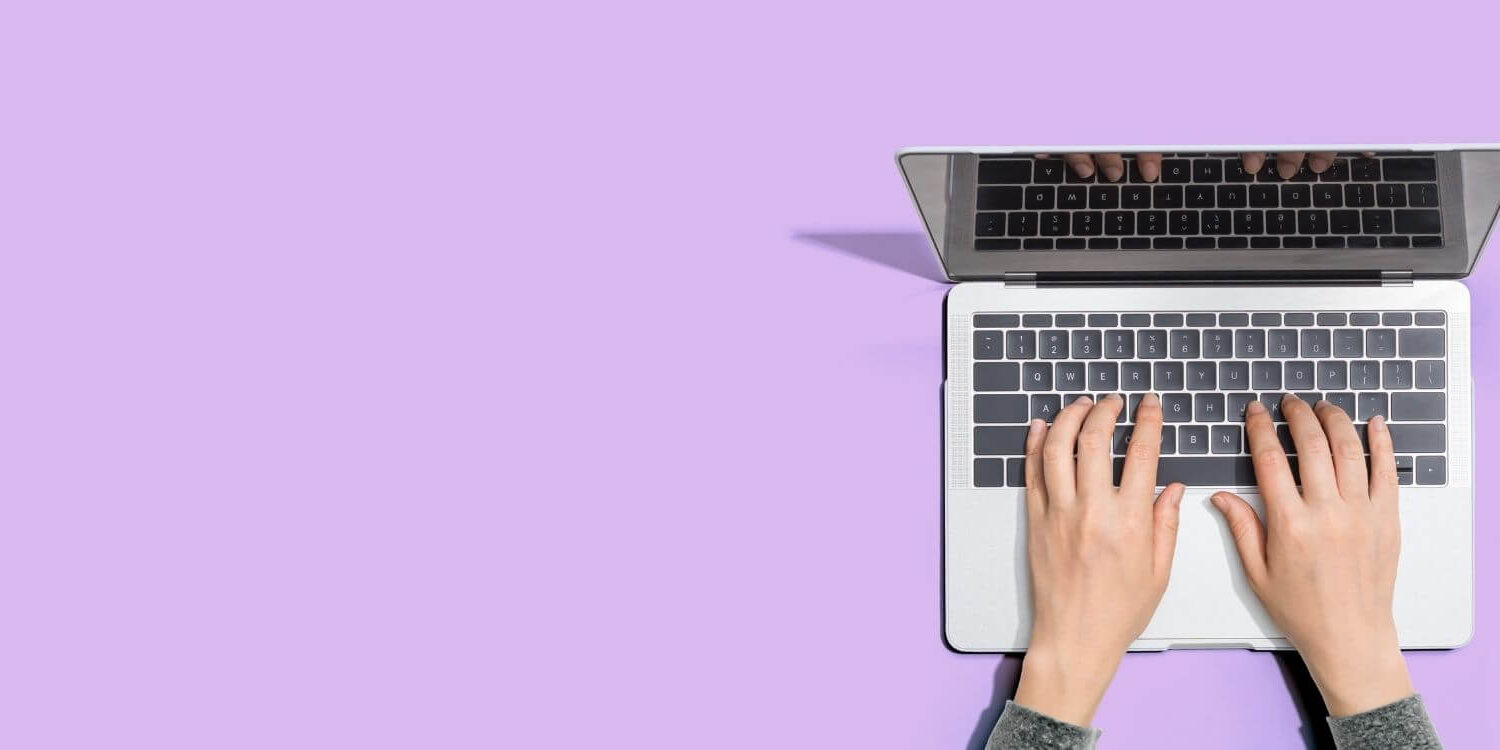purple desk with a laptop and woman's hands typing