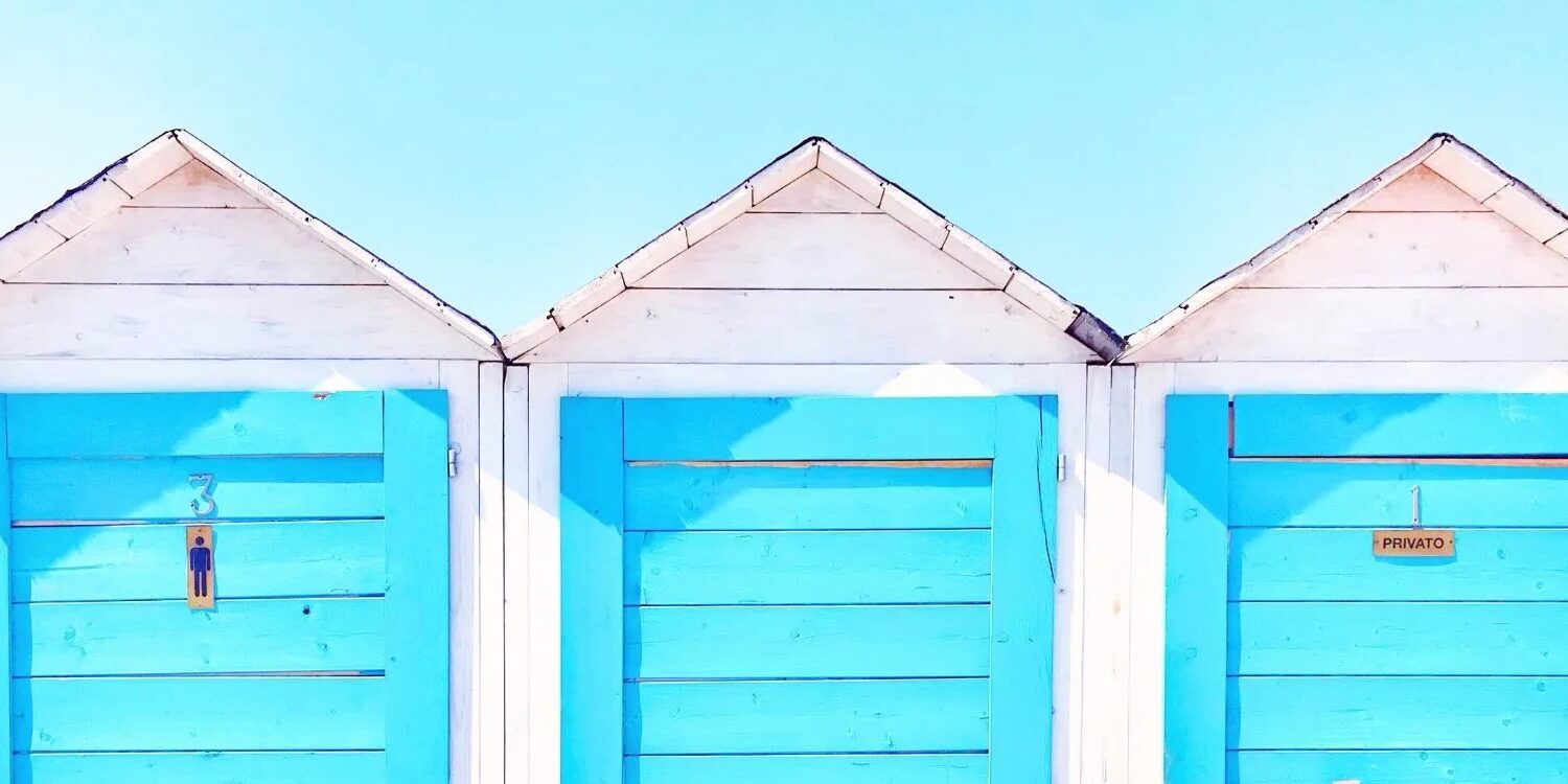 three beach changing rooms with white siding and blue doors. behind them is a blue sky