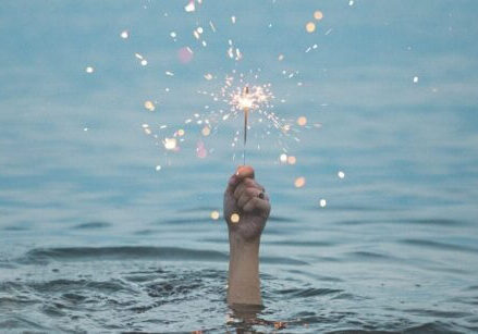 woman's hand holding a sparkler above the surface of the water