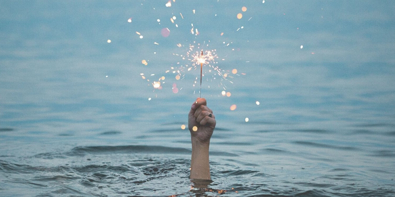 woman's hand holding a sparkler above the surface of the water