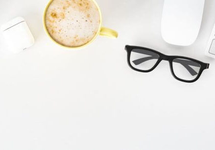high-key flat lay of a desk with a keyboard, mouse, cappuccino, plant, and eyeglasses