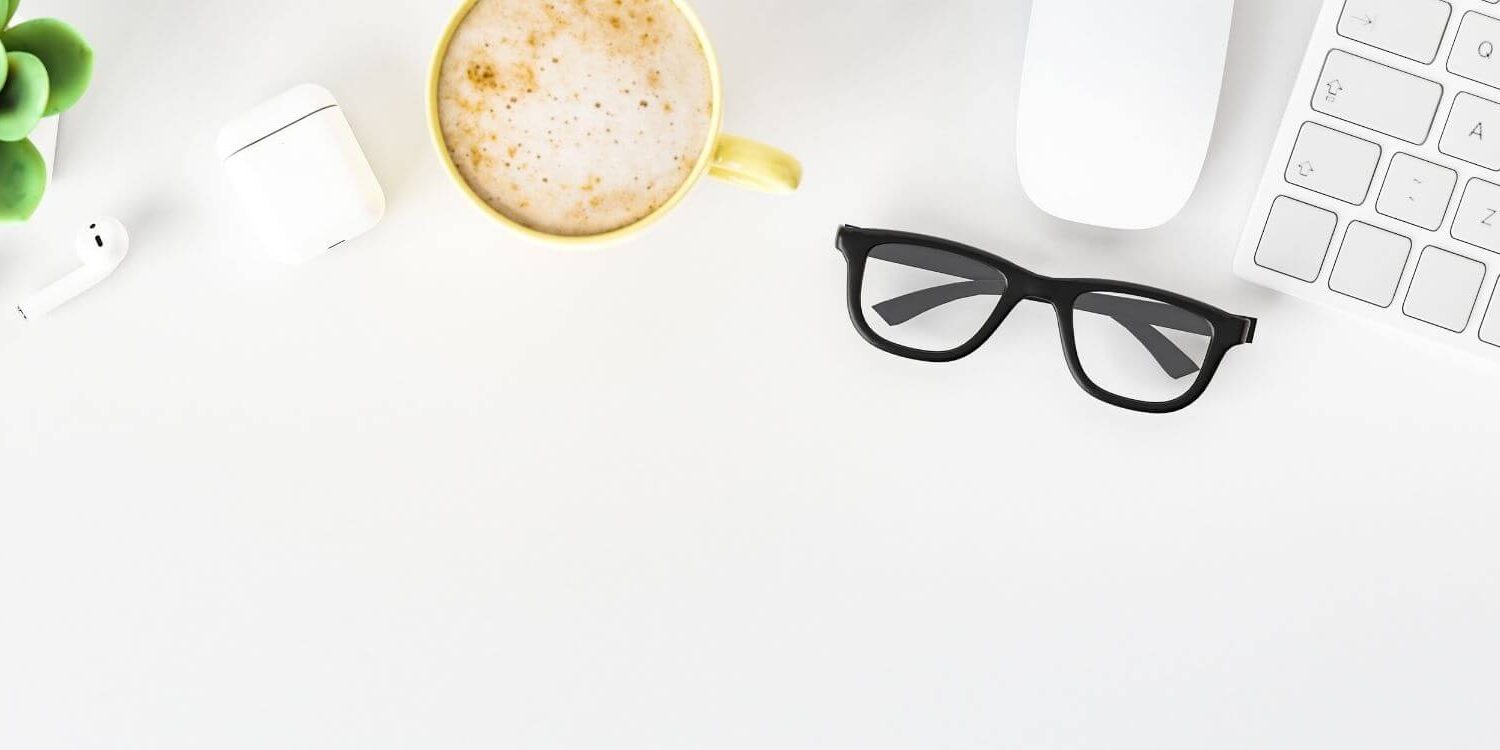 high-key flat lay of a desk with a keyboard, mouse, cappuccino, plant, and eyeglasses