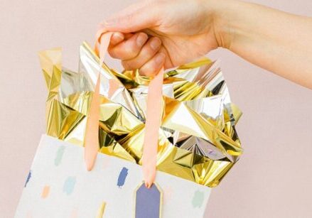 person holding a gift bag with gold tissue for blog post "9 No-Cost and Low-Cost Ways to Show Your Clients Love & Appreciation"