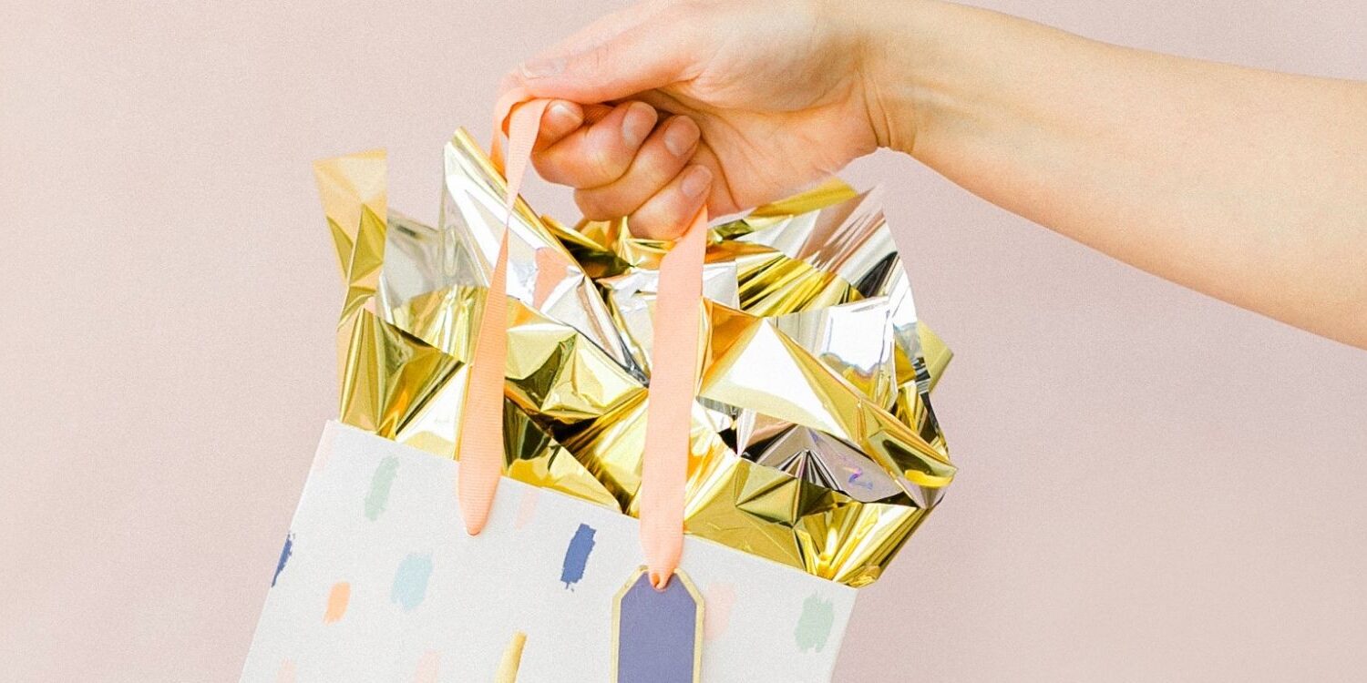 person holding a gift bag with gold tissue for blog post "9 No-Cost and Low-Cost Ways to Show Your Clients Love & Appreciation"