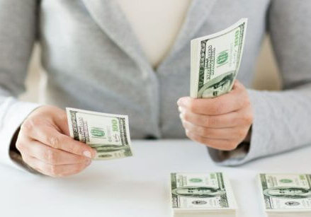 woman wearing a gray sweater counting money into piles on a desk