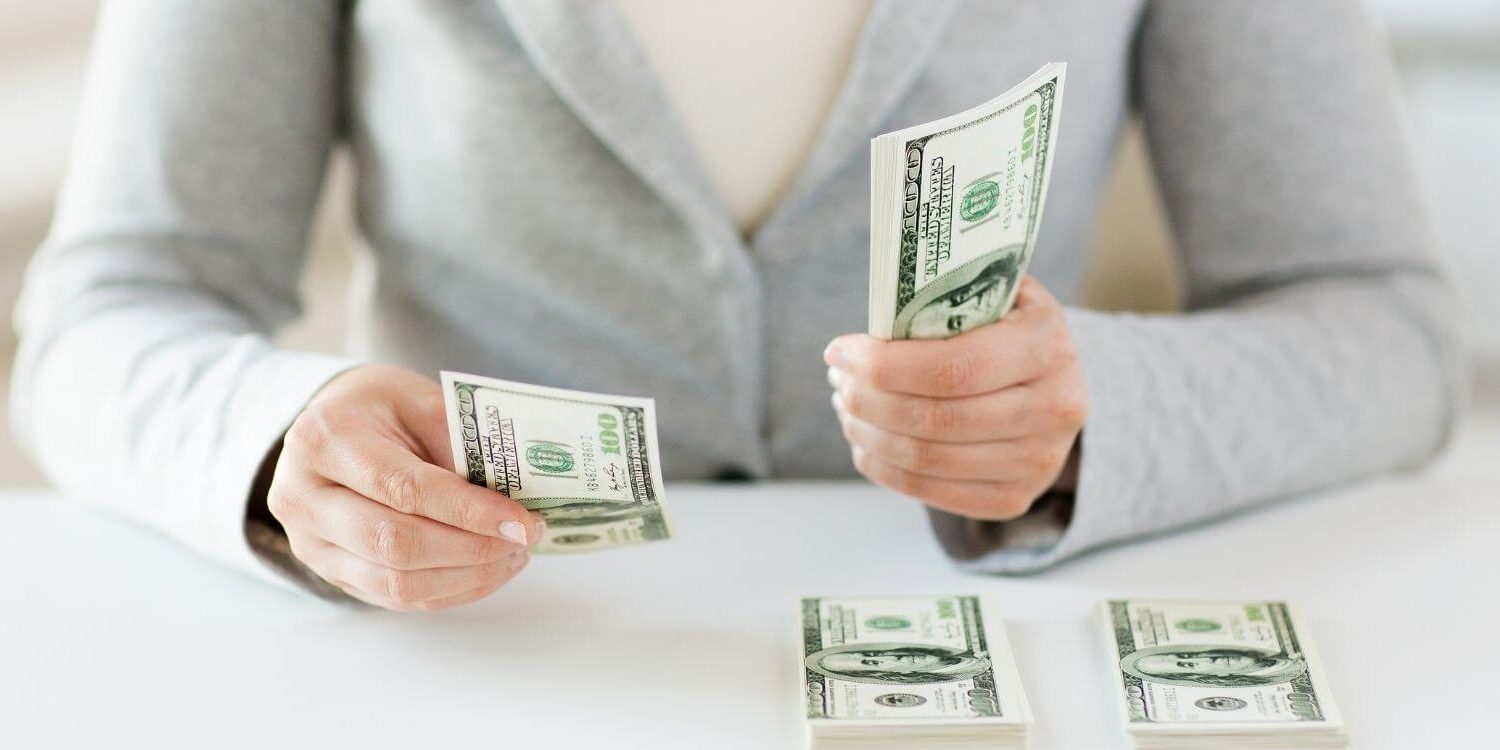 woman wearing a gray sweater counting money into piles on a desk