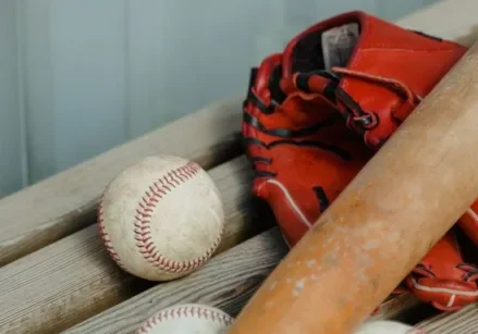 red baseball glove with a wooden bat and baseballs on a bench