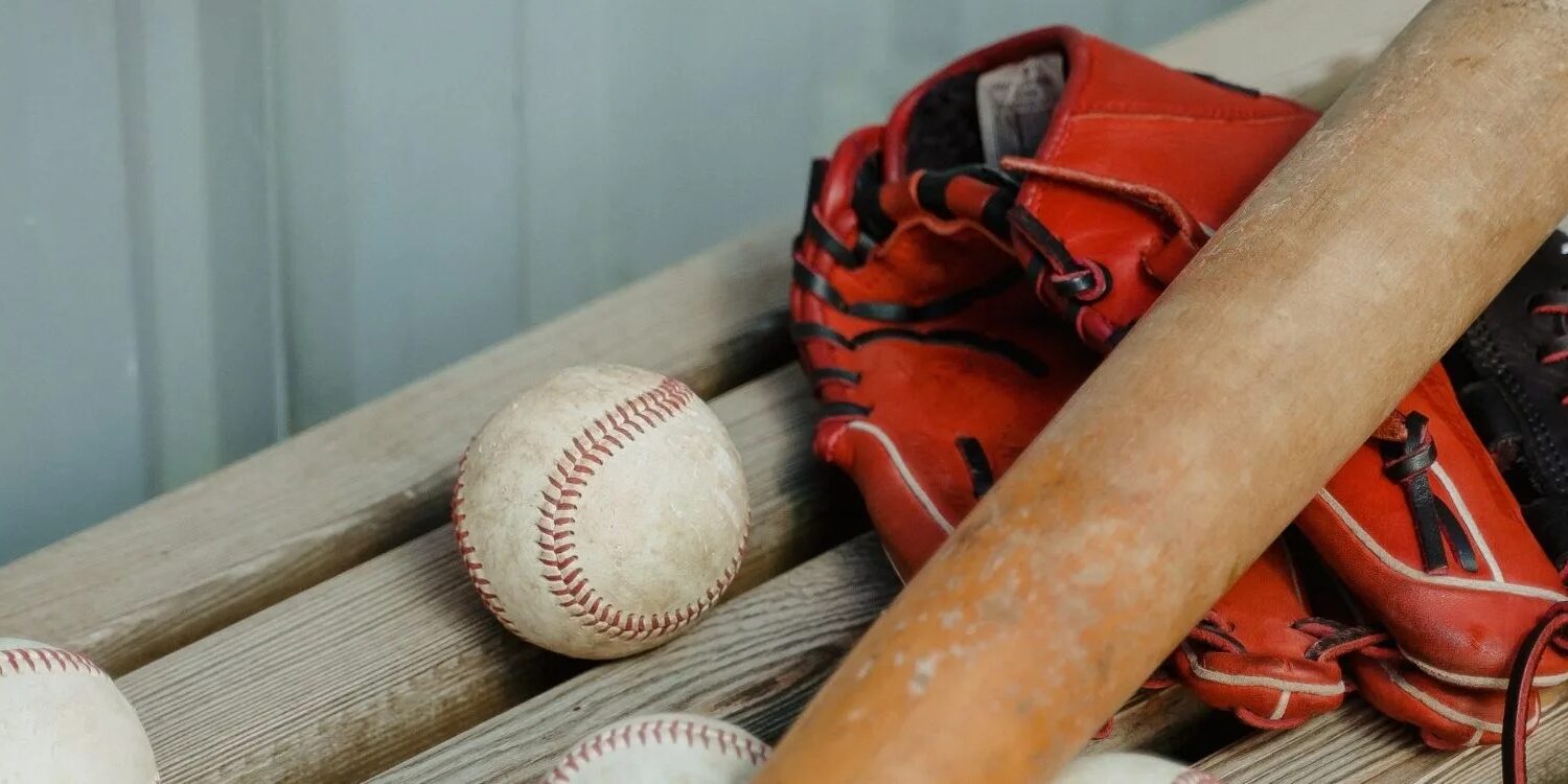 red baseball glove with a wooden bat and baseballs on a bench