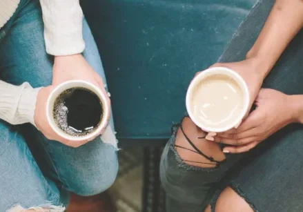 photo of the laps of two women in jeans holding coffee