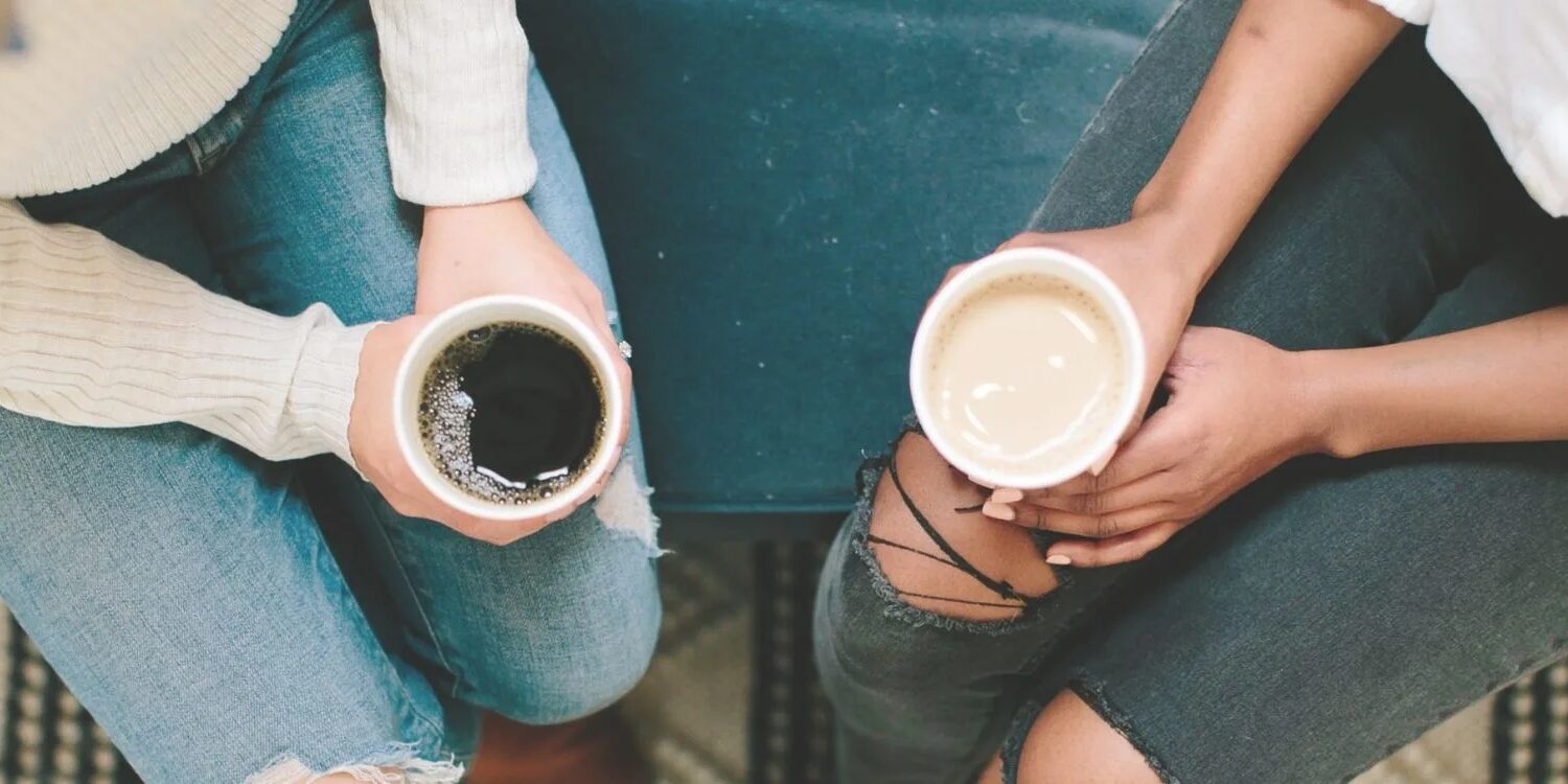 photo of the laps of two women in jeans holding coffee